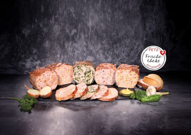 Fleischkäse-Sortiment auf schwarzer Platte mit angeschnittenen Scheiben, Zwiebel, Brötchen, Senf, Knoblauch, Petersilie und grüner Paprika; daneben Logo „PETZ Frischetheke“.